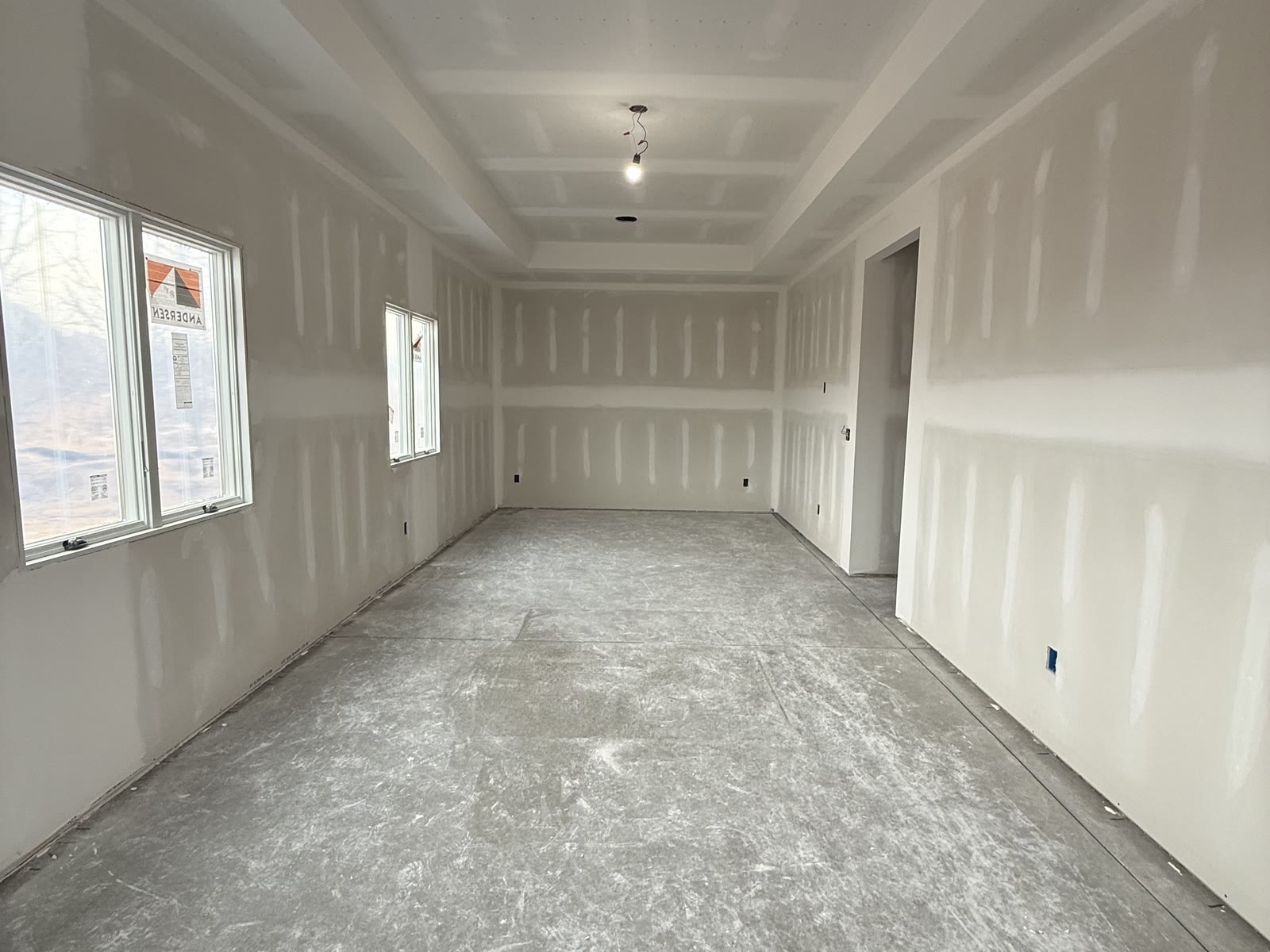 Long room with coated drywall seams, a stepped ceiling, three windows, and an open doorway
